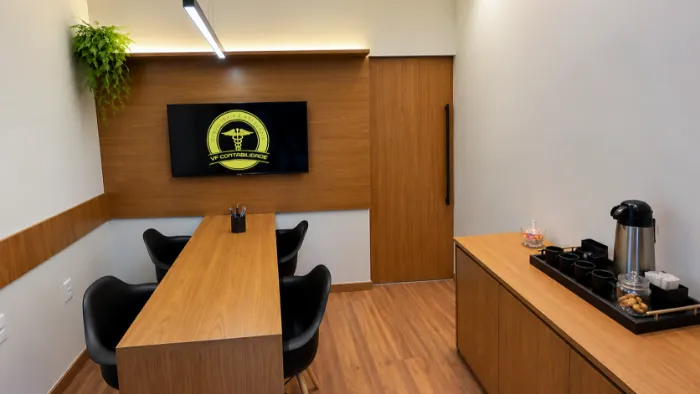 Sala de reunião da VF Contabilidade com mesa de madeira, cadeiras pretas, televisor com a logomarca e bancada de café
